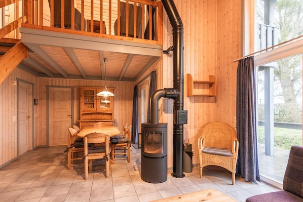 Interior acogedor de una cabaña con comedor, un gran hogar de leña negra y un balcón con barandas de madera.