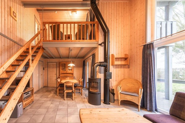 L’intérieur d’un chalet en bois comprend un escalier, un coin repas, un canapé et une grande fenêtre.