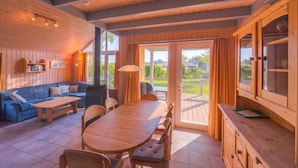 Une pièce chaleureuse avec un plafond en bois, un canapé bleu, une table à manger en bois et une grande fenêtre donnant sur un paysage verdoyant.