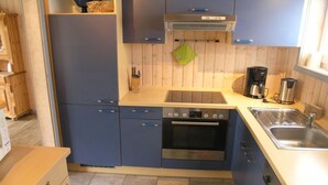 Una cocina compacta con armarios azules, un horno Bosch, una cafetera y un lavamanos.