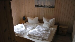 Un dormitorio con paneles de madera, una cama, almohadas, una mesita de noche y un cuadro de veleros.
