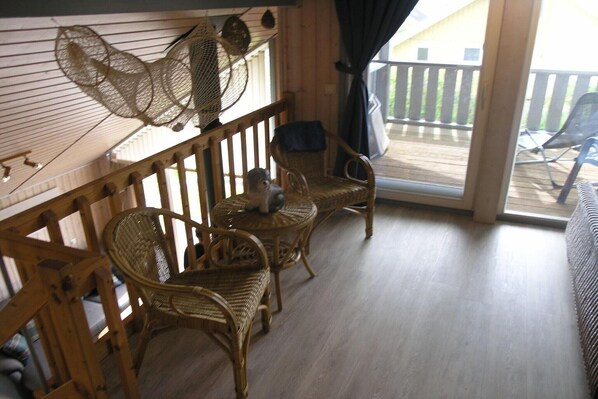 A balcony with wicker furniture, a wooden railing, and a view of the outside deck.
