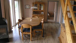 Una mesa de comedor de madera con sillas, un armario de madera y una escalera en una habitación con paredes y suelos de madera.