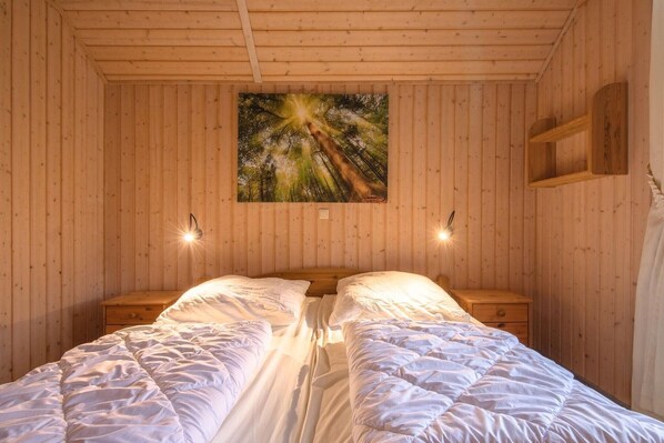 A wooden-paneled room with a bed, two bedside tables, and a wall-mounted picture. - Ferienhaus im skandinavischen Stil (Rechlin)