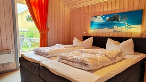 Ein Schlafzimmer mit zwei Betten, Holzwänden, einem Bild von einem Baum an einem Strand und einem Fenster mit Vorhängen.
