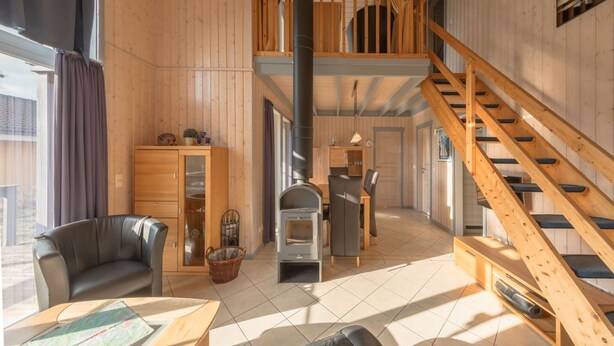 A spacious room with a wooden interior, a fireplace, a dining area, and a staircase. - Ferienhaus im Ferienpark Mueritz (Rechlin)