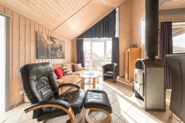 A cozy cabin with a wooden interior, a sofa, two chairs, a small table, and a wood stove.