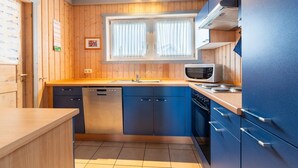 Une cuisine de taille réduite avec des murs en bois, une fenêtre avec des rideaux, un four à micro-ondes et un lave-vaisselle.