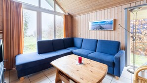 Un salon moderne avec un canapé d’angle bleu, une table basse en bois et une grande fenêtre avec des rideaux.