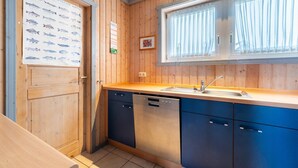 Une cuisine de taille réduite avec des murs en bois, une grande fenêtre avec des rideaux, un évier et un lave-vaisselle.