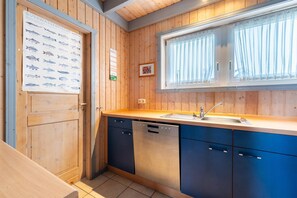 A compact kitchen with wooden walls, a large window with curtains, a sink, and a dishwasher. - Ferienhaus im Ferienpark Mueritz (Rechlin)