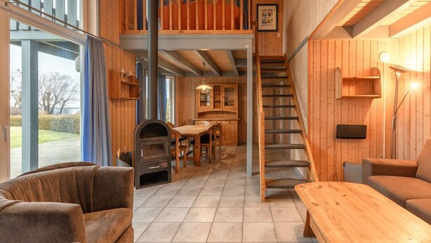 A spacious living area with a high ceiling, wooden walls, a staircase, and a view of the outdoors. - perfektes Ferienhaus für Familien (Rechlin)