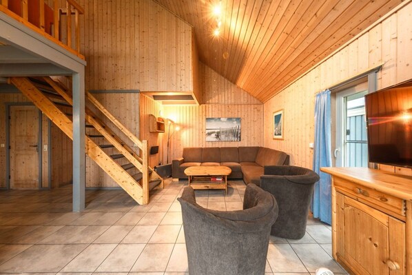 Een houten interieur met een trap, een bank, een bijzettafeltje en een televisie.