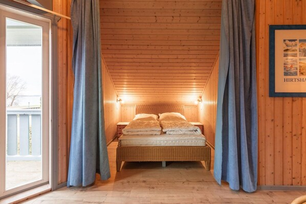 A wooden cabin bedroom with a bed, curtains, and a framed picture on the wall.