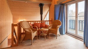 A cozy wooden room with wicker furniture, a large window, and a view of the outdoors. - perfektes Ferienhaus für Familien (Rechlin)