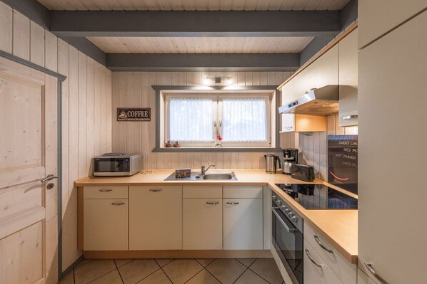 Una cocina compacta con microondas, lavabo y estufa. Un cartel sobre la ventana dice "COFFEE".