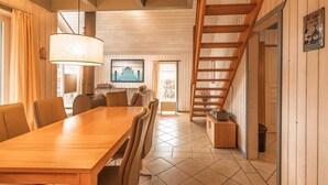A spacious dining area with a long wooden table and chairs, a hanging light fixture, and a staircase leading to an upper level. - exklusives skandinavisches Ferienhaus (Granzow)