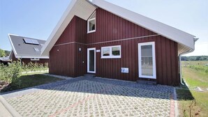 A modern red building with a sloped roof, a paved entrance, and a small parking sign. - Ferienhaus im skandinavischen Stil (Granzow)