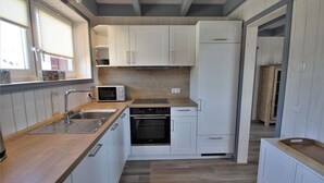 A compact kitchen with white cabinets, a microwave, a stove, and a sink. - Ferienhaus im skandinavischen Stil (Granzow)