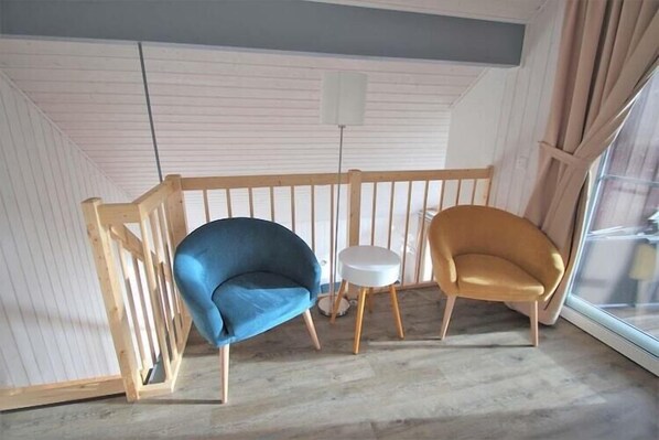 A room with a wooden railing, two chairs, a small round table, and a floor lamp.