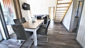 Ein modernes Hotelzimmer mit einem Holztisch, schwarzen Stühlen, einem Flachbildfernseher und einer Treppe.