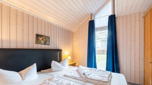 Ein Zimmer mit Holzwänden, einem Bett, einem Nachttisch und einem Fenster mit Vorhängen.