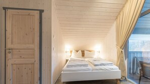 A bedroom with a wooden ceiling, a bed with white bedding, a wooden door, and a view of the outdoors through a window. - exklusives skandinavisches Ferienhaus (Granzow)