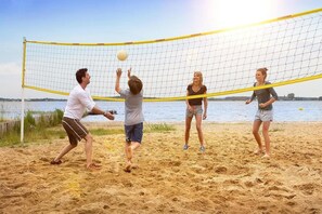 A group of people playing beach volleyball on a sandy beach with a body of water in the background. - Ferienwohnung im Ferienpark Mueritz (Rechlin)