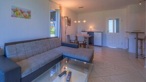 Ein Wohnzimmer mit Sofa, einem Glastisch und einer Küche im Hintergrund.