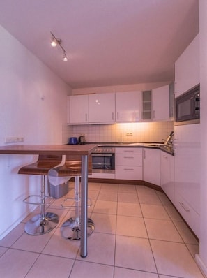 A compact kitchen with white cabinets, a wooden countertop, and a built-in oven. - Ferienwohnung im Ferienpark Mueritz (Rechlin)