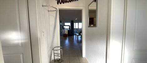 Un couloir avec une pancarte « Bienvenue », un présentoir métallique et une vue sur un espace de vie doté d’une grande fenêtre.