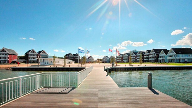 A waterfront property with a wooden pier leading to a dock, surrounded by multi-story buildings with flags. - liebevoll eingerichtetes Appartement (Rechlin)