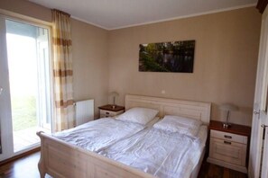 Une chambre à coucher avec un lit double, une table de chevet avec une lampe, un radiateur et une fenêtre avec des rideaux.