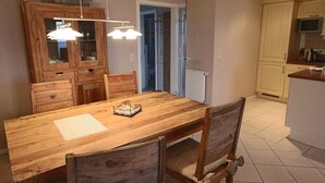 Een eetgedeelte met een houten tafel en stoelen, een kast met glazen deuren, en een keuken met kastjes en een magnetron.