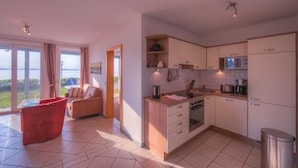 A modern kitchen with white cabinets, a microwave, and a sink. There is a red chair and a sofa in the living area.