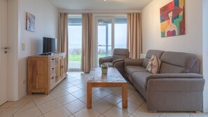 Una sala de estar con un sofá, una mesa de centro, un televisor sobre un mueble de madera y un cuadro en la pared.