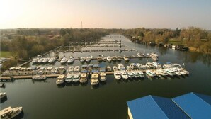 Un puerto deportivo con numerosas embarcaciones amarradas en aguas tranquilas, rodeado de árboles y terreno abierto.
