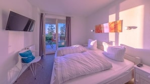 A bedroom with a bed, a TV mounted on the wall, and a window with curtains.