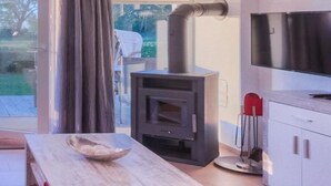 A modern kitchen with a built-in wood stove, a dining table with a bowl, and a TV mounted on the wall.