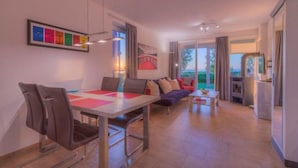A modern living room with a dining area, a sofa set, a TV, and a view of the outdoors.