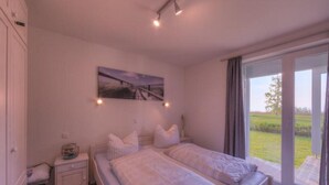 A bedroom with a bed, a nightstand, a painting, and a view of a garden through a sliding door. - tolles Appartment in der Seenplatte (Rechlin)