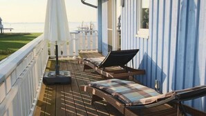A deck with two lounge chairs and a white umbrella, overlooking a grassy area and water.