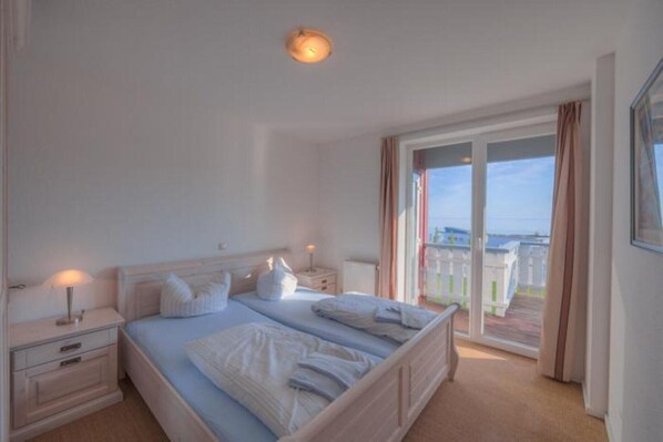 A bedroom with a large bed, bedside tables, a nightstand, and a view of the outside through a sliding glass door. - exklusives Appartement in Rechlin (Rechlin)