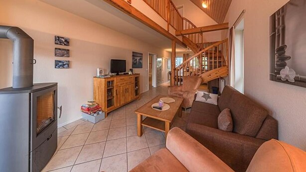 A spacious living area with a fireplace, wooden furniture, and a staircase leading to an upper level. - Appartement im Ferienpark in Rechlin (Rechlin)