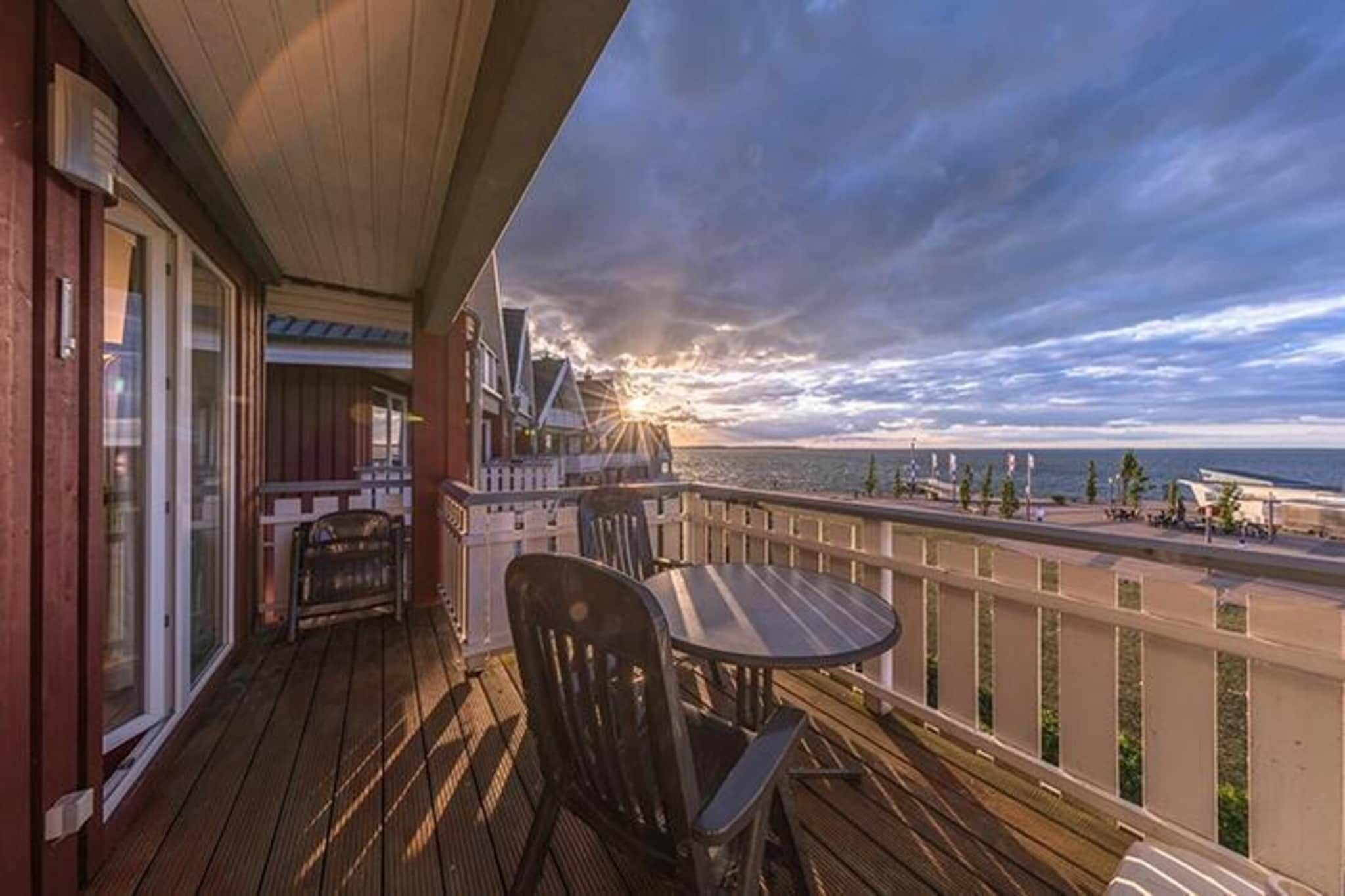 Una terraza de madera con una mesa y sillas, con vista a una playa al atardecer.