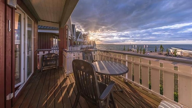Une terrasse en bois avec une table et des chaises, donnant sur une plage où l’on peut admirer le coucher de soleil.