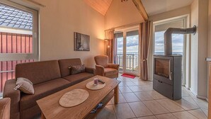 A cozy living room with a sofa, armchairs, a wooden coffee table, and a wood-burning stove. - Appartement im Ferienpark in Rechlin (Rechlin)