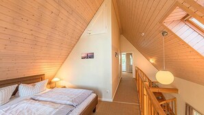 A bedroom with a sloped ceiling, a bed, a nightstand, and a staircase leading to an upper level. - Appartement im Ferienpark in Rechlin (Rechlin)