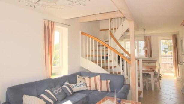 A living room with a blue sofa, a wooden staircase, and a dining area. - liebevoll eingerichtetes Apartement (Rechlin)