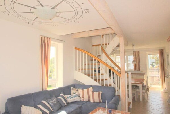A living room with a blue sofa, a wooden staircase, and a dining area.